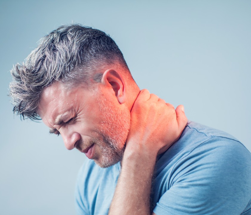A man in a blue shirt is holding his neck, displaying signs of discomfort against a soft blue background.