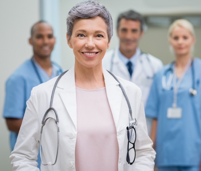 A medical professional in a white coat stands confidently, surrounded by colleagues in scrubs, conveying teamwork in a healthcare setting.