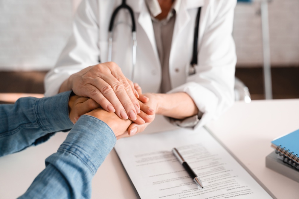 A doctor in a white coat gently holds a patient hands